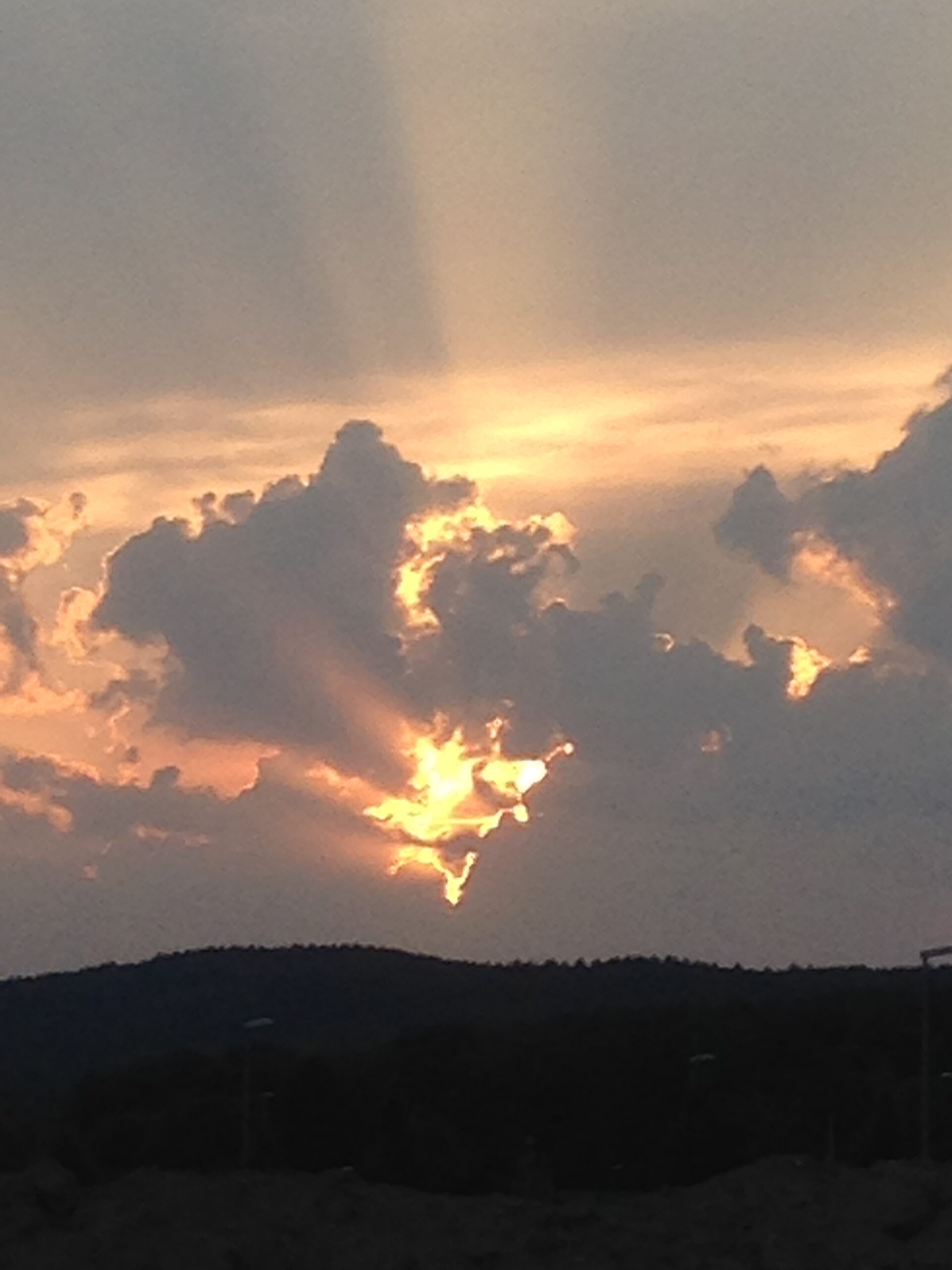 „Sonnenlicht bricht durch dunkle Wolken über einer Landschaft.“